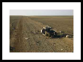 Junked car rests near a primitive desert road