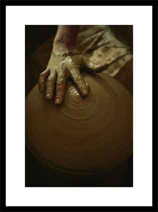 Close-up of the brown muddy hand of a potter as he spins a clay pot on his wheel